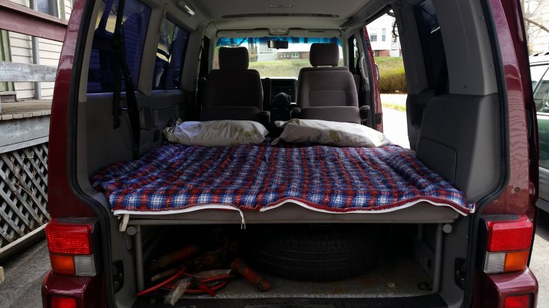 Grey interior of a burgundy Volkswagen Eurovan with a sleeping bag, one of the most important van life accessories.