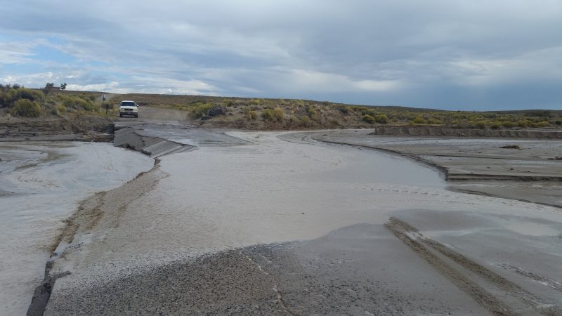 A badly flooded road with a white truck attempting to pass.