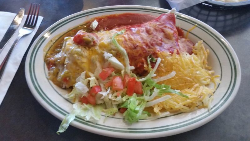 A breakfast burrito smothered in red and green chile and chees, with hash browns and lettuce and tomatoes from one of the most popular places to eat in Albuquerque for diner-style food.