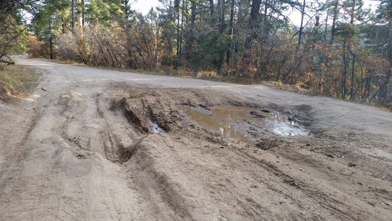 A very badly rutted dirt road with a mud puddle in the middle.