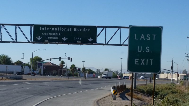A green sign with white lettering stating last U.S. exit before driving to Baja California from Calexico to Mexicali.