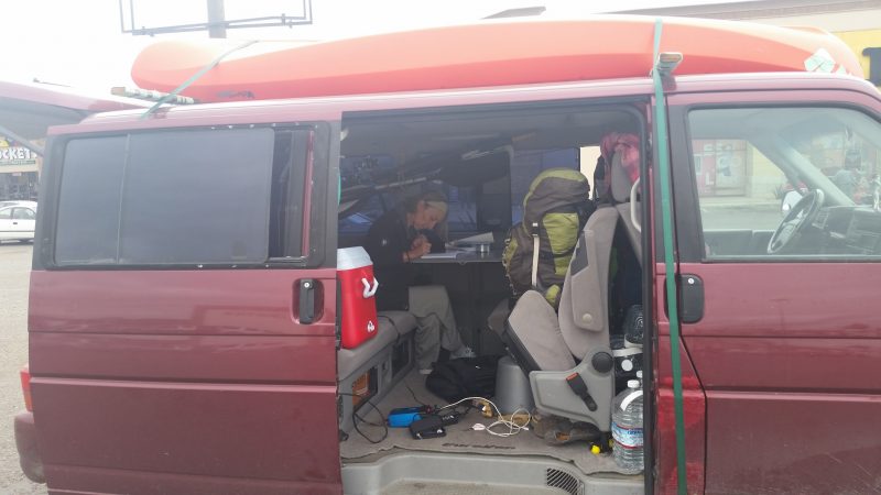 A burgundy Volkswagen van with side door open and a woman writing inside.