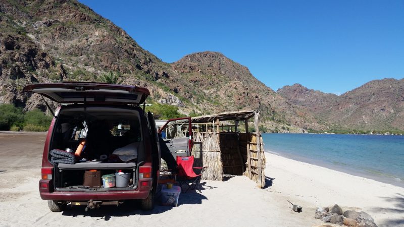 A Volkswagen van Baja California camping on a white sand beach with mountains in the background.