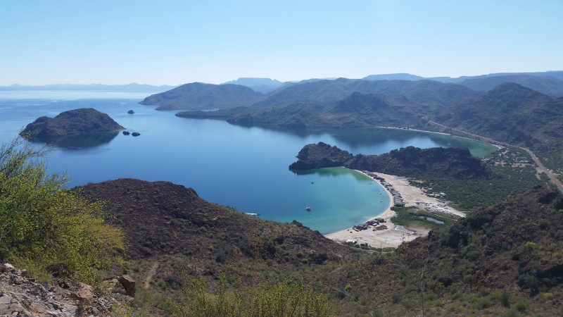 A view of two beaches with white sand and blue water full of people camping in Baja California.