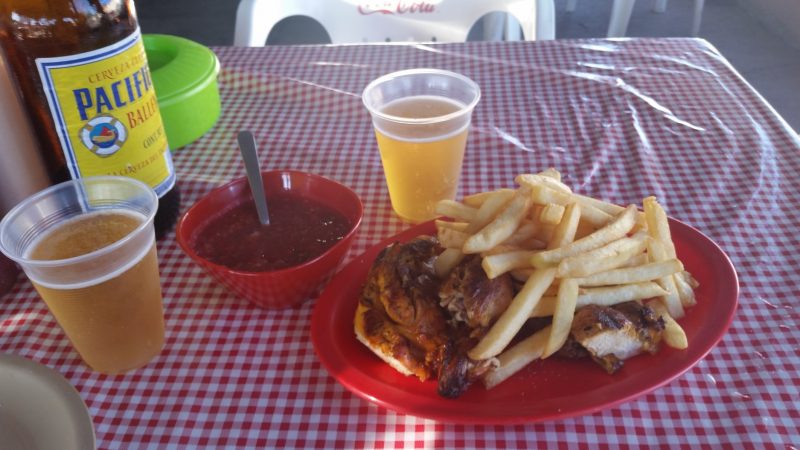 A plate of roast chicken with French fries and beer on a gingham tablecloth at a restaurant on the Baja Peninsula in Mexico.