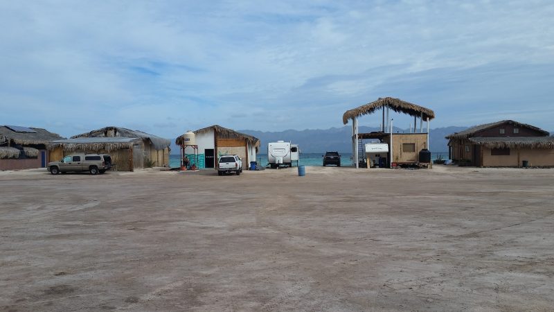 Several beach palapas sheltering trucks and RVs which are Baja California camping for the season.