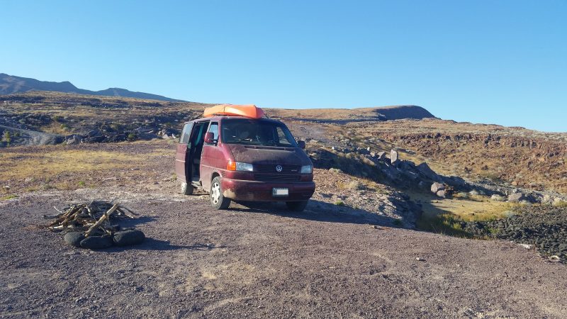 A maroon Volkswagen van with orange kayak on the roof parked on scenic overlook during a Baja California road trip.