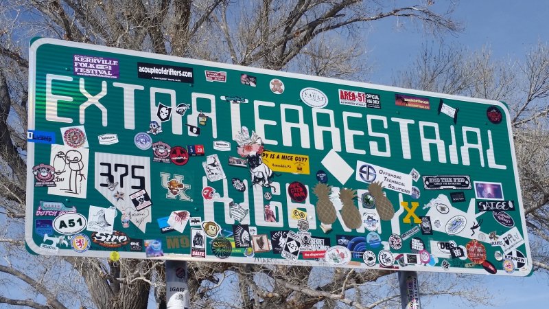 An official green Extraterrestrial Highway sign in Nevada full of many colorful bumper stickers.