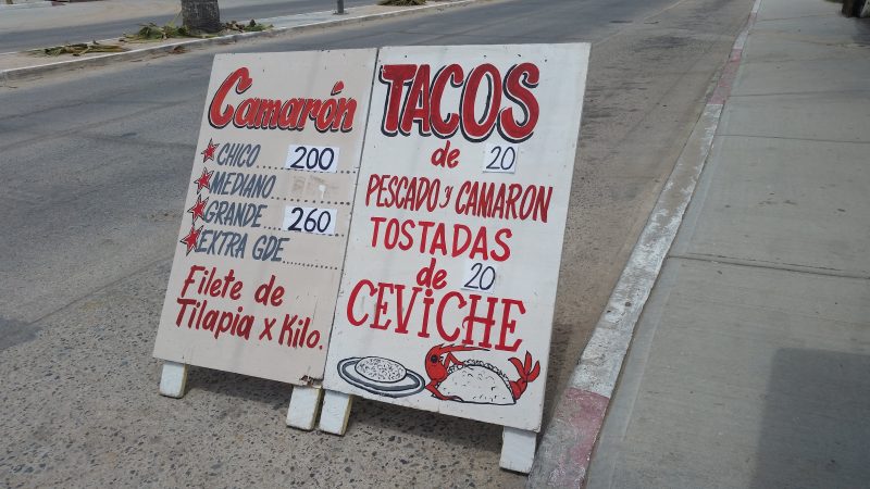 Red writing on a white sandwich board sign advertising fish tacos in a small town located in Baja California Sur, Mexico.