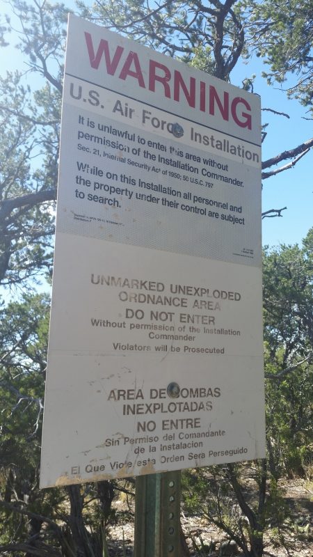A white warning sign announcing a U.S. air force installation on a hiking path.