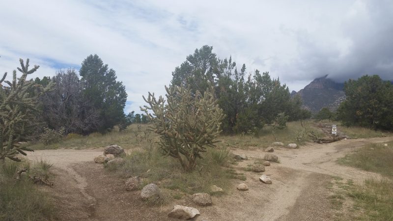 A junction of 3 hiking trails in the foothills of Albuquerque against a cloudy sky.