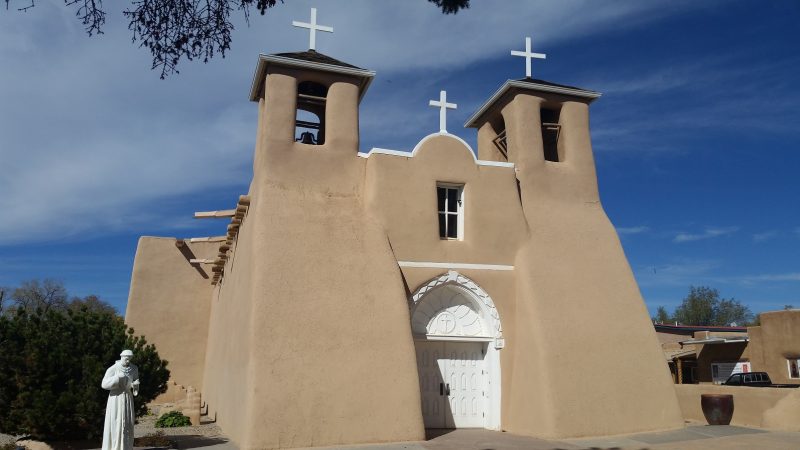 An adobe church near Taos, New Mexico with a white door against a blue sky.