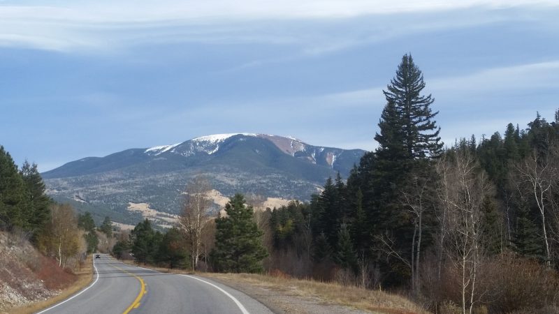 A winding road with pine trees on the side and a snow capped mountain on the Enchanted Circle Scenic Byway, a New Mexico scenic drive near Taos.