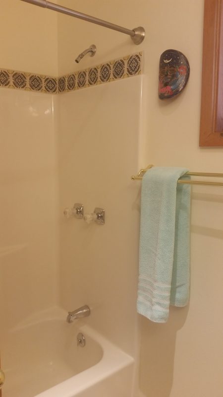A shower with a towel rack holding a green bath towel.