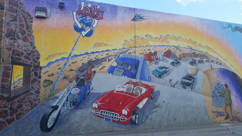 A painted mural of Route 66 with a red sports car and a homeless person pushing a shopping trolley.