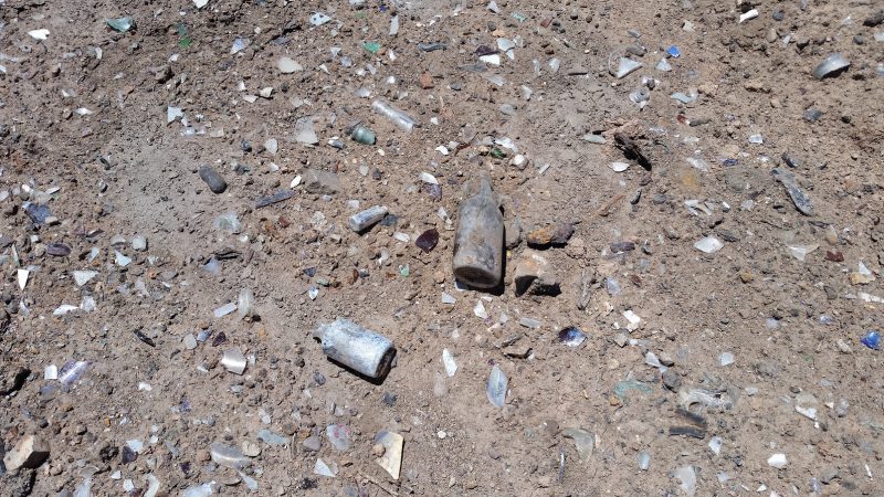 Old oxidised glass bottle, both complete and broken laying in dirt at the glass graveyard in Albuquerque.
