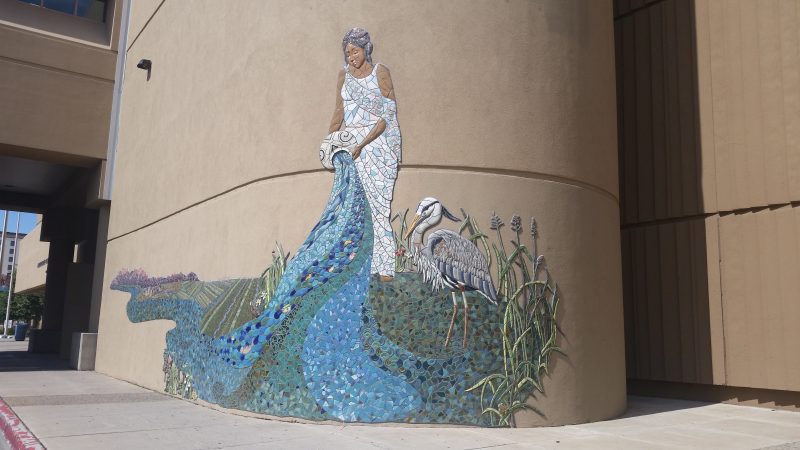 A mosaic on the facade of a building in downtown Albuquerque, New Mexico of a Native American woman pouring water from an urn with a white heron or crane beside her.