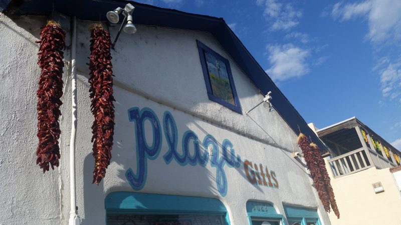 The Plaza Gifts building in Old Town Albuquerque, painted in blue on white with two red chile ristras hanging from the gable.