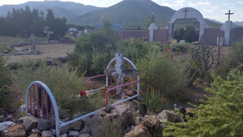 A graveyard in front of a church overgrown with weeds and cactus on the Turquoise Trail in New Mexico.