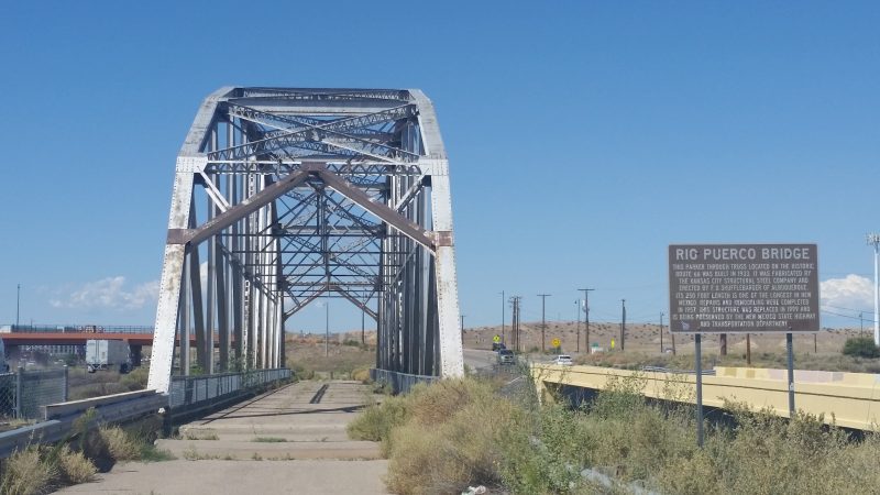 Old silver, steel-beamed bridge with traffic passing by on either side.