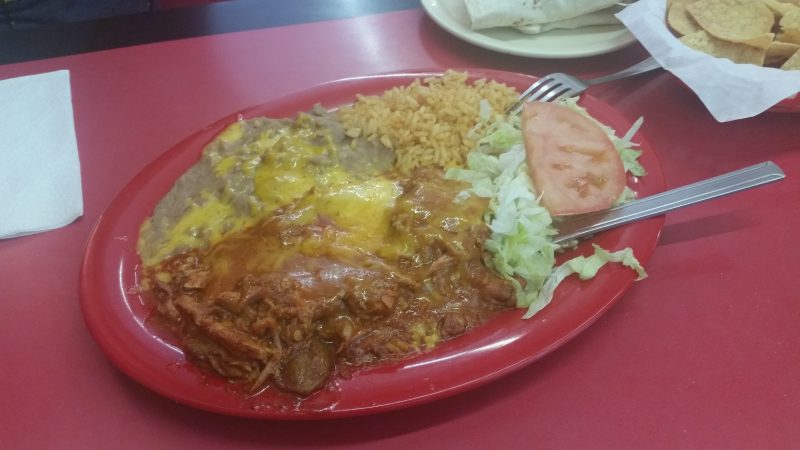 Cheese covered carne adovada, rice and beans with lettuce and tomato on a red plate from El Sabor de Juarez Mexican restaurant in Albuquerque.
