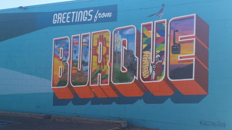 Blue wall painted with colourful mural saying Greetings from Burque.