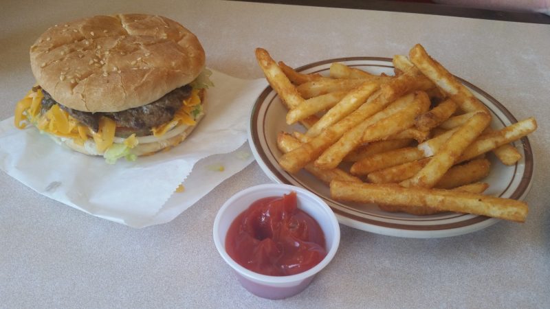 A burger, fries and a cup of ketchup on a plain table.