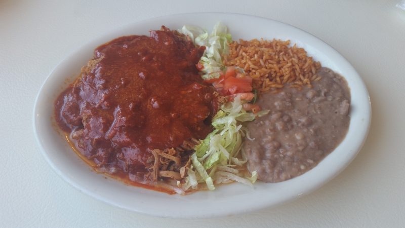 A plain white oval plate full of refried beans, rice, salad and shredded pork in a adovada red chile sauce from Mary and Tito's Cafe in Albuquerque.