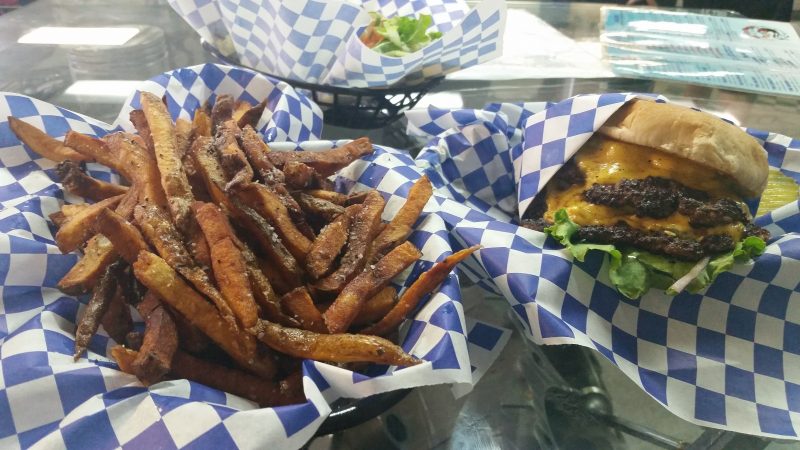 Two burger baskets lined with blue and white-checkered paper holding french fries and a green chile cheeseburger from Dia de los Takos in Albuquerque, New Mexico.