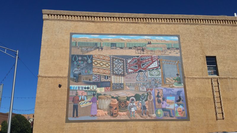 Colourful mural of Navajo traders and Navajo rugs on yellow brick building.