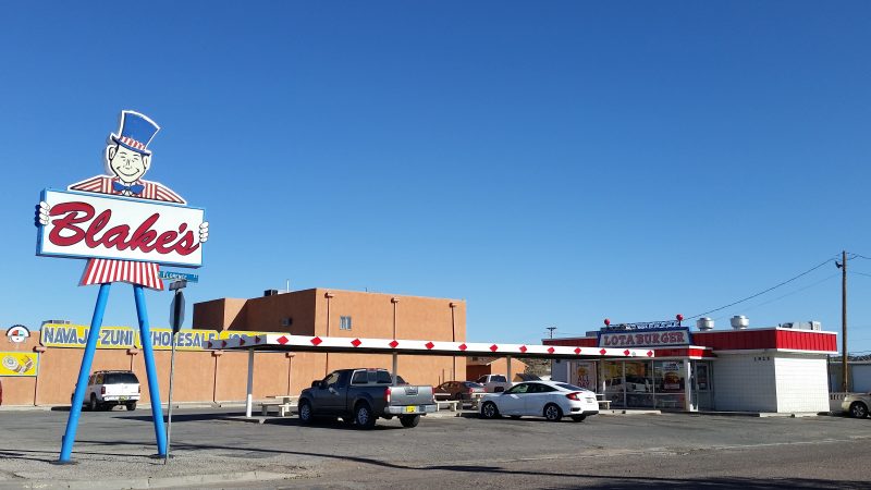 Tall sign of a man in a red and white striped jacket and blue top hat holding a sign advertising Blake's Lotaburger, one of the most recognized places to eat in Albuquerque.