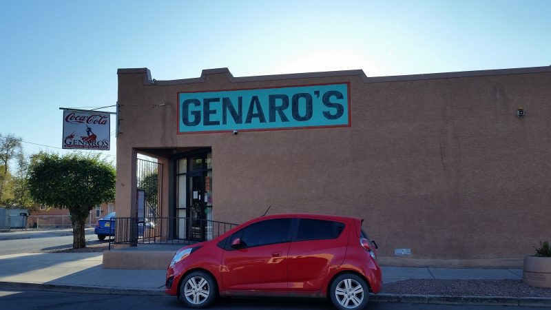 A red compact car in front of an adobe restaurant with a blue sign on the side.