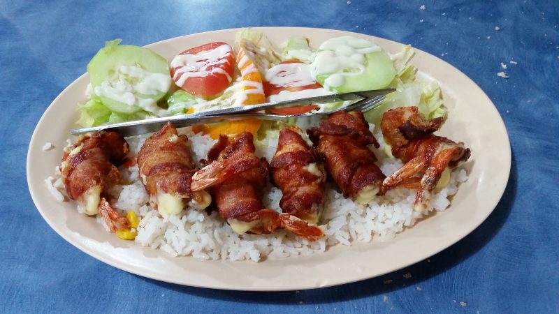 A plate of bacon-wrapped shrimp and salad on a blue table top.