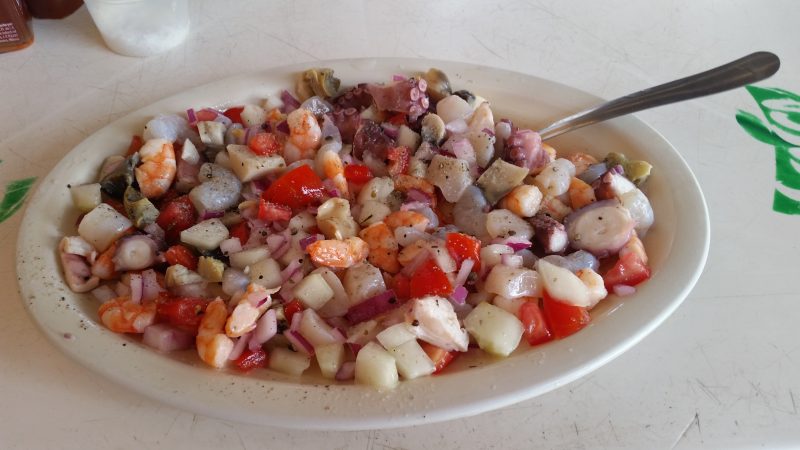 A white oval plate of assorted shellfish cooked ceviche style, sitting on a white table top.