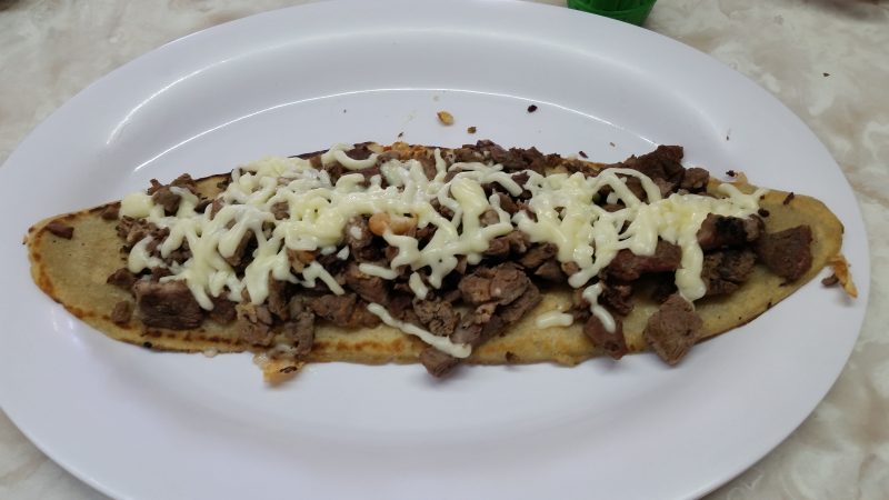 A huarache, one of the lesser-known Mexican street foods, topped with carne asada and melted Chihuahua cheese.