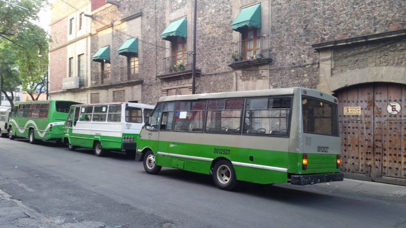 Green buses parked in front of an old stone building.