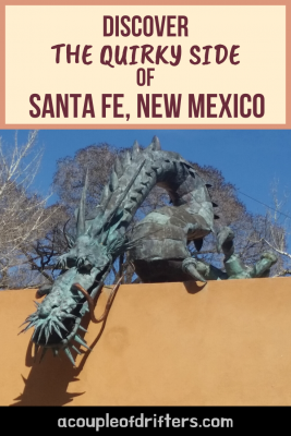 A tarnished copper statue of a dragon peering over the edge of a building with a blue sky in the background in Santa Fe, New Mexico.