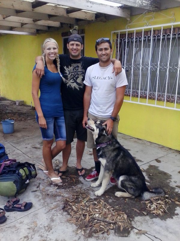 Three people and a dog in front of a yellow house.