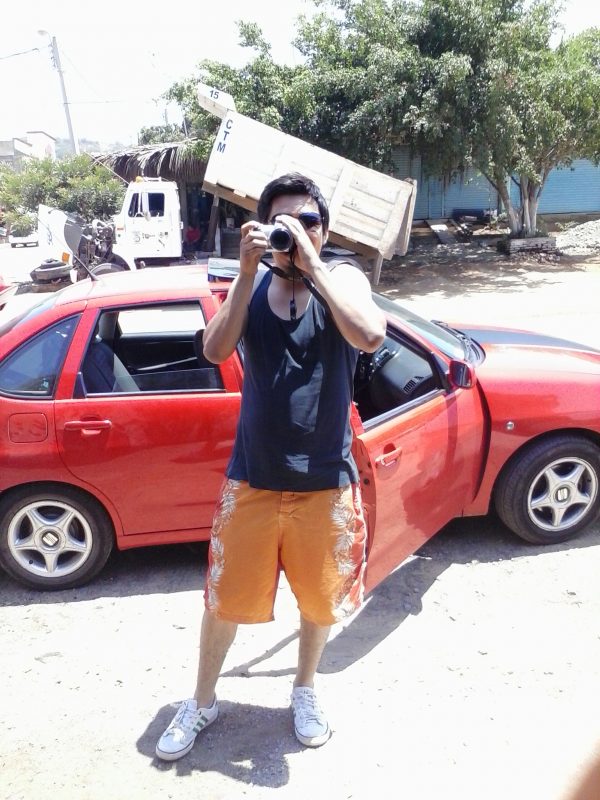 Man with camera in front of a red car.